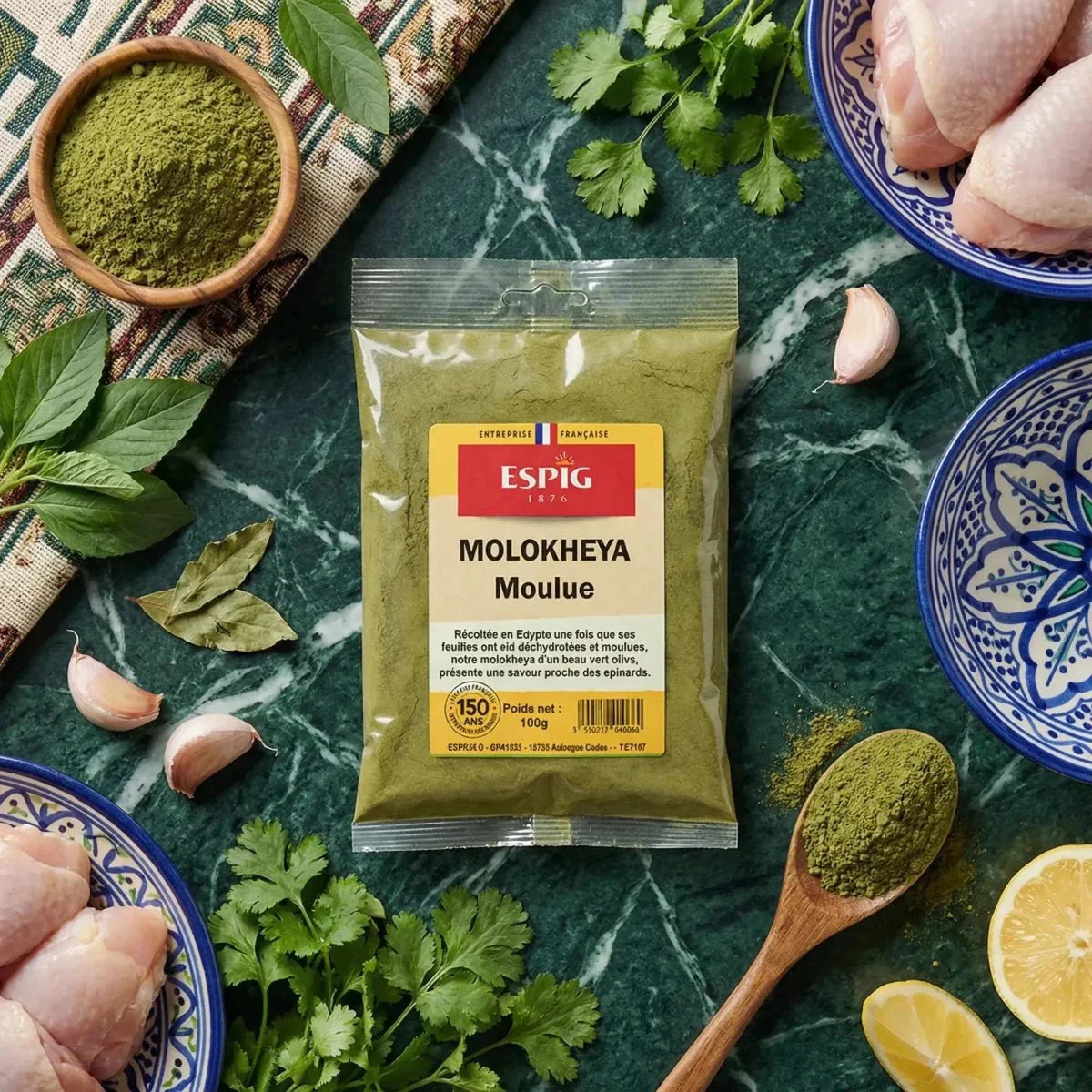 Sachet Molokheya moulu ESPIG, 100g, entouré d'ingrédients : poulet, citron, ail, herbes.
