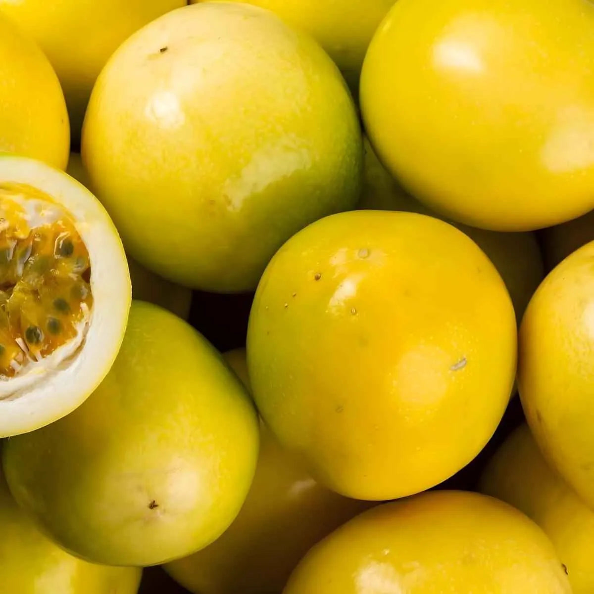 Gros plan de fruits de la passion jaunes entiers et coupés, ingrédient principal du Nectar Passion MONTPELÉ, saveur tropicale intense.