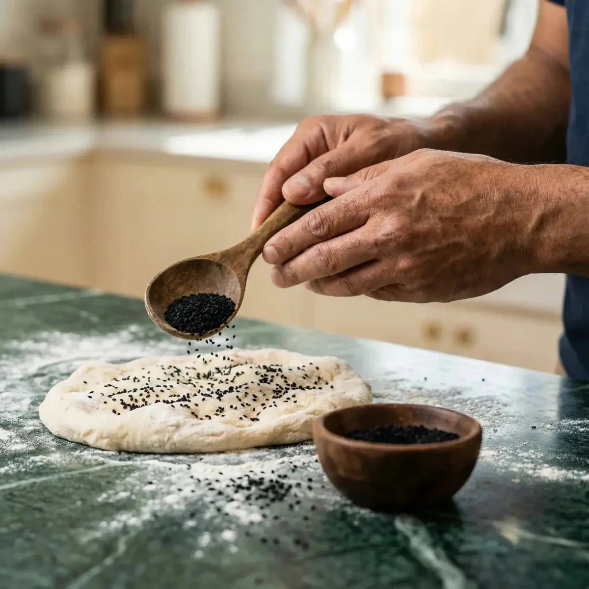 Semi di nigella SAMIA cosparsi su una pasta per pane. Mani che tengono un cucchiaio di legno.