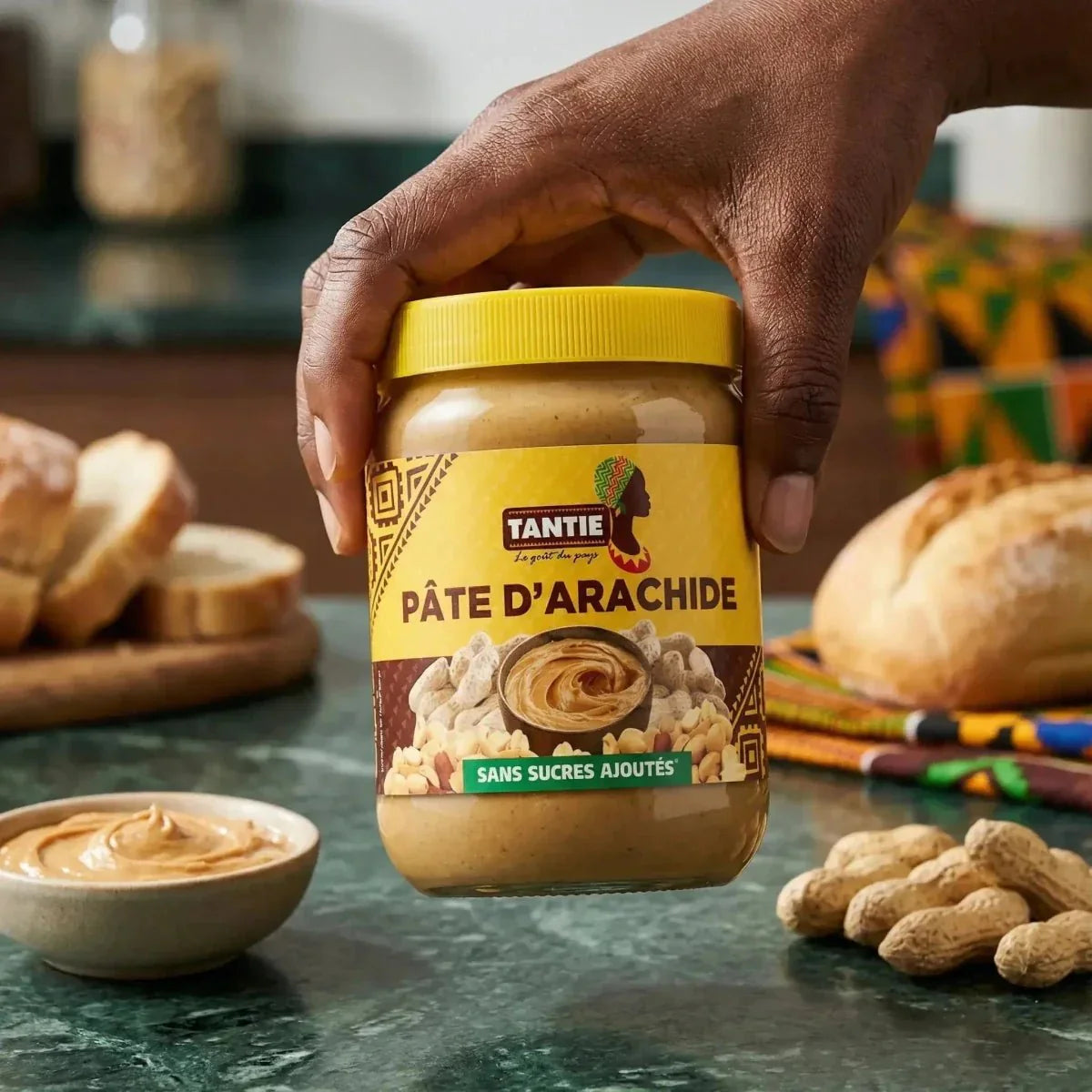 Cremige Erdnussbutter von TANTIE, mit ganzen Erdnüssen, gelbes Glas in der Hand gehalten.