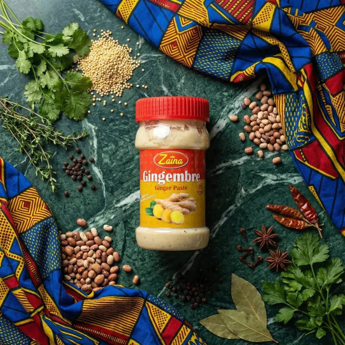 ZAINA Ingwerpaste (750g) auf marmoriertem Hintergrund mit Gewürzen und buntem afrikanischem Stoff.