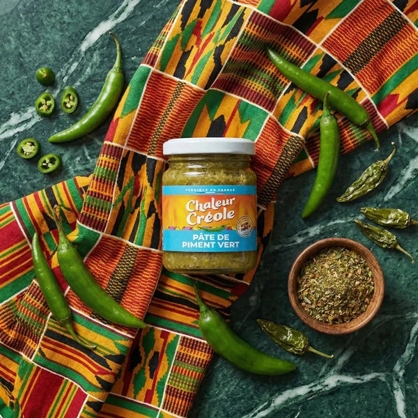 Pâte de piment vert CHALEUR CRÉOLE sur une table avec piments verts frais, séchés et épices.