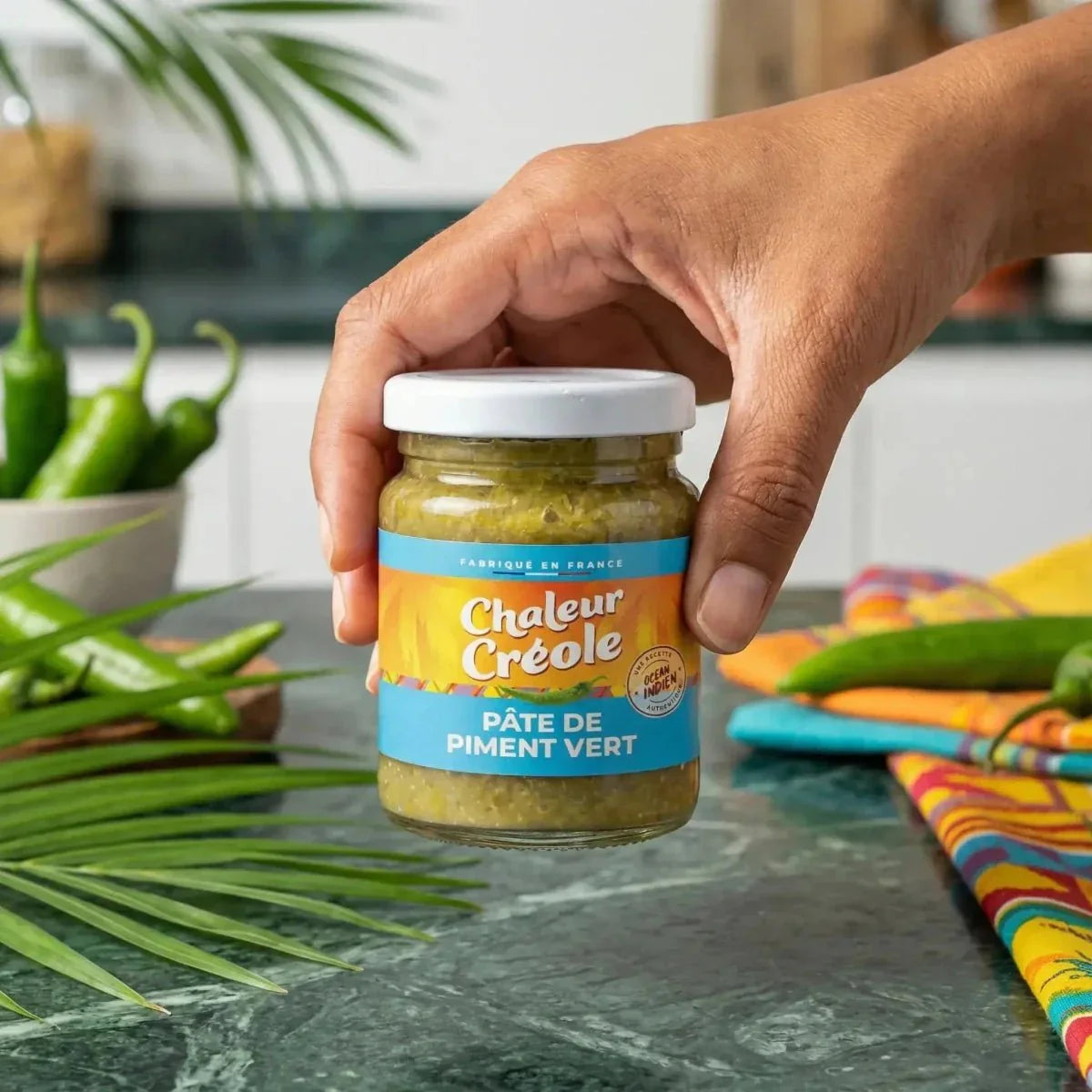 Green chili paste by CHALEUR CRÉOLE, in a glass jar, with a hand holding the jar.