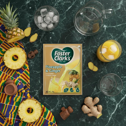 Sachet de jus poudre ananas gingembre FOSTER CLARKS entouré d’ingrédients frais sur fond marbré. Boisson pratique et fruitée à reconstituer.
