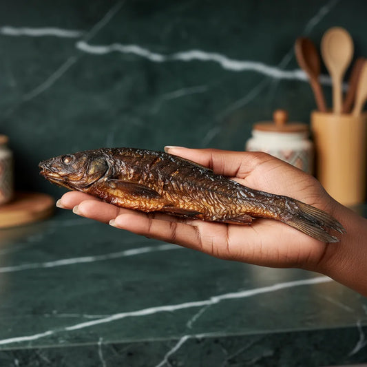 Chinchard fumé entier tenu à la main, mettant en valeur sa texture authentique pour une cuisine traditionnelle aux saveurs marines.