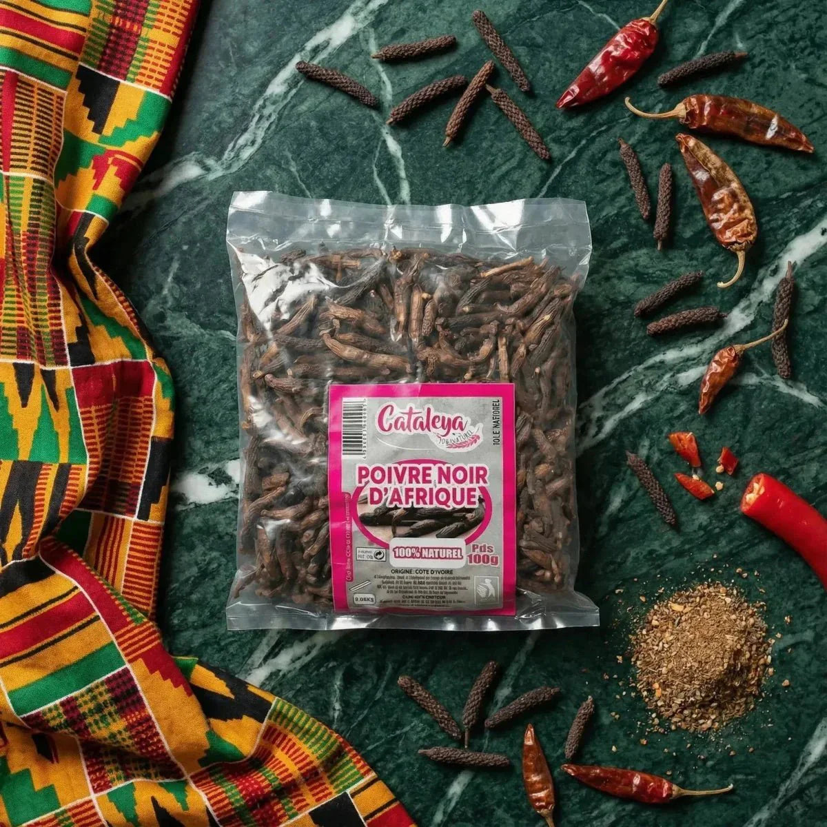 Poivre noir d'Afrique CATALEYA en sachet, piments rouges et tissu coloré sur fond vert marbré.