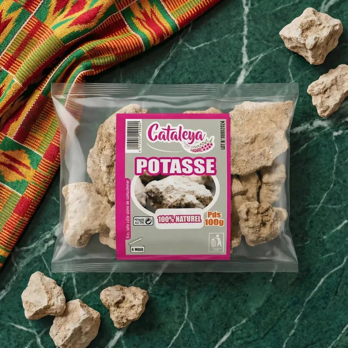 Beutel mit Pottasche CATALEYA (100g) auf einem Marmortisch, bunter Stoff im Hintergrund.