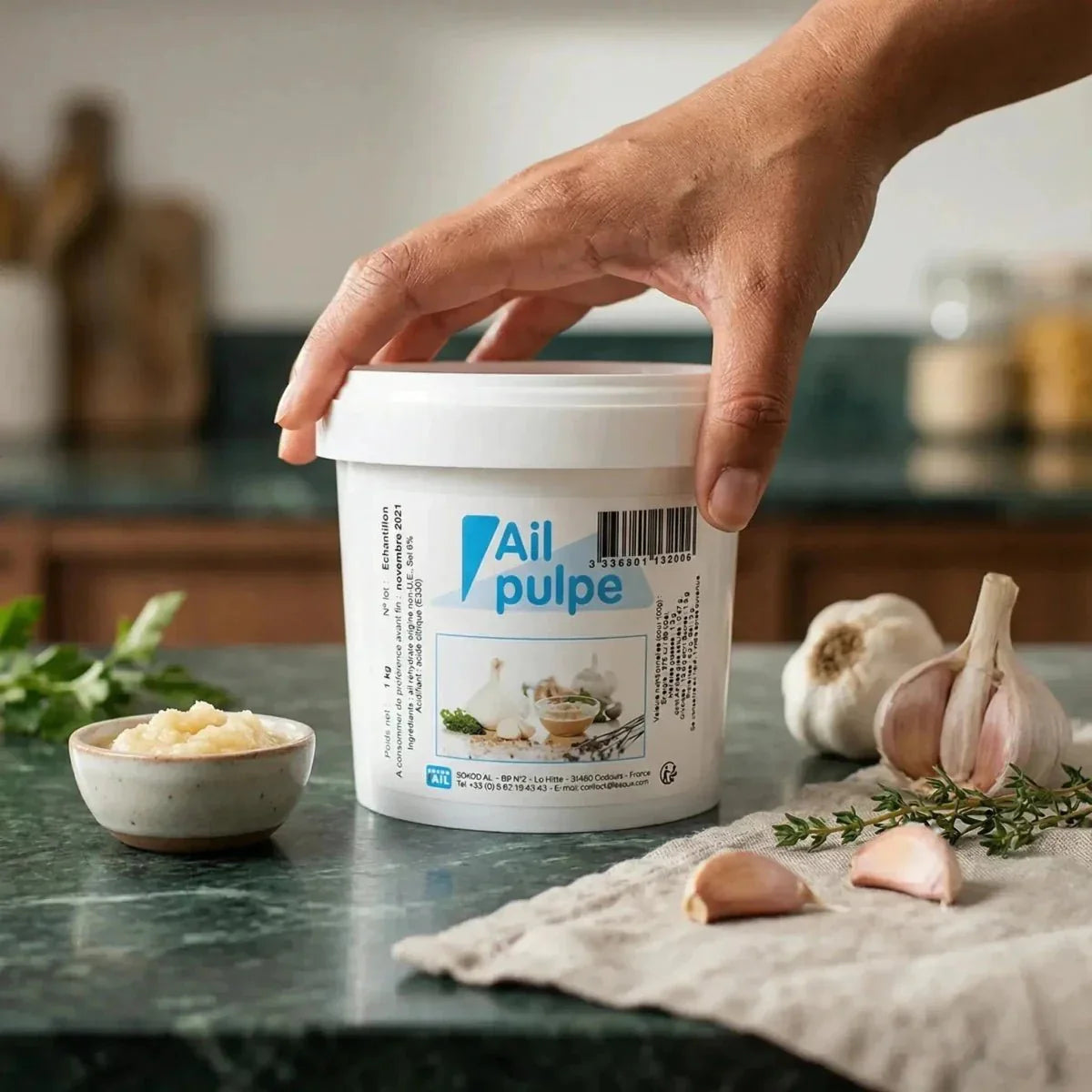 Polpa d'aglio, di SOKOD'AIL, in un barattolo bianco, presentata con spicchi d'aglio.