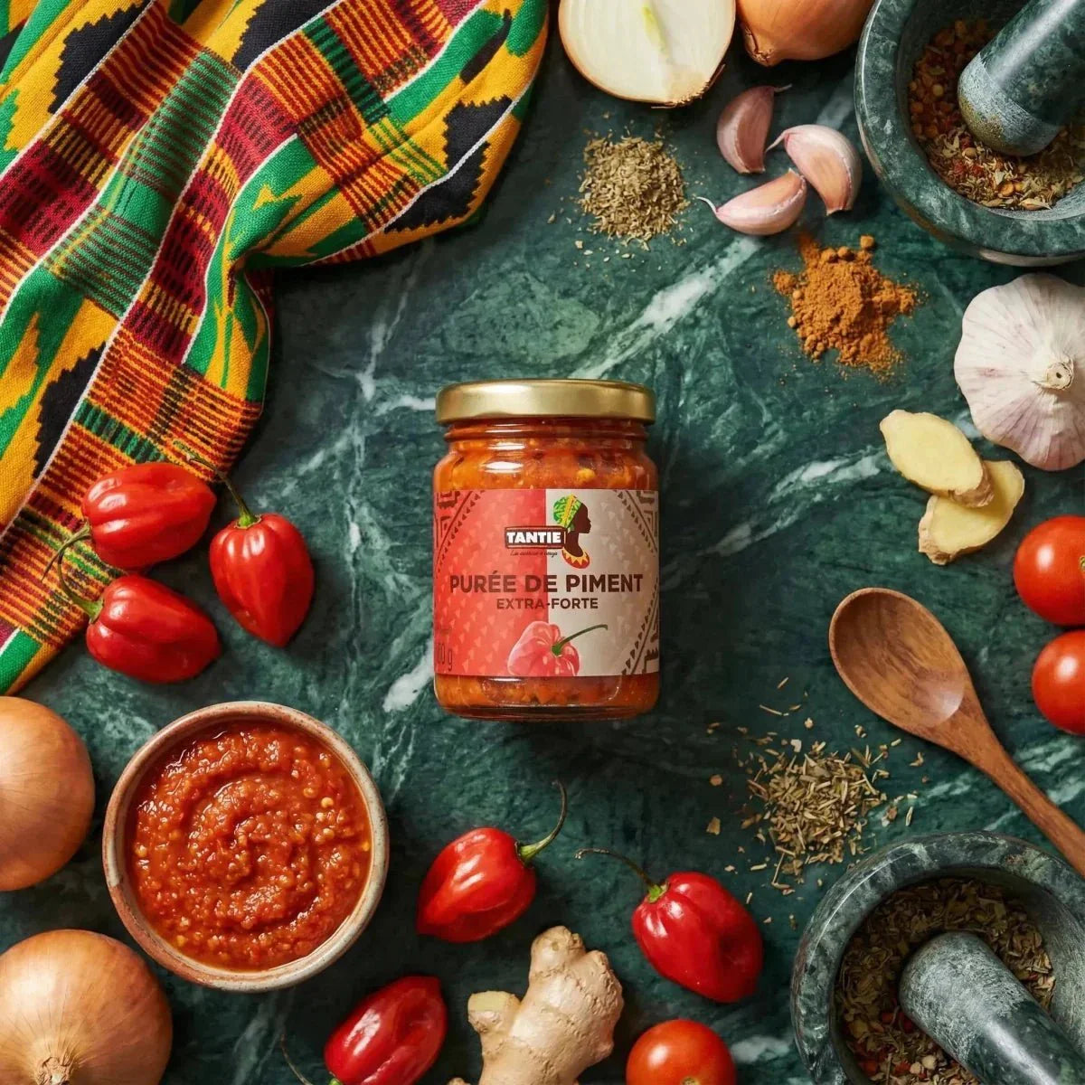 Purea di peperoncini extra piccante TANTIE 100g, ingredienti freschi, mortai e tessuto africano colorato.