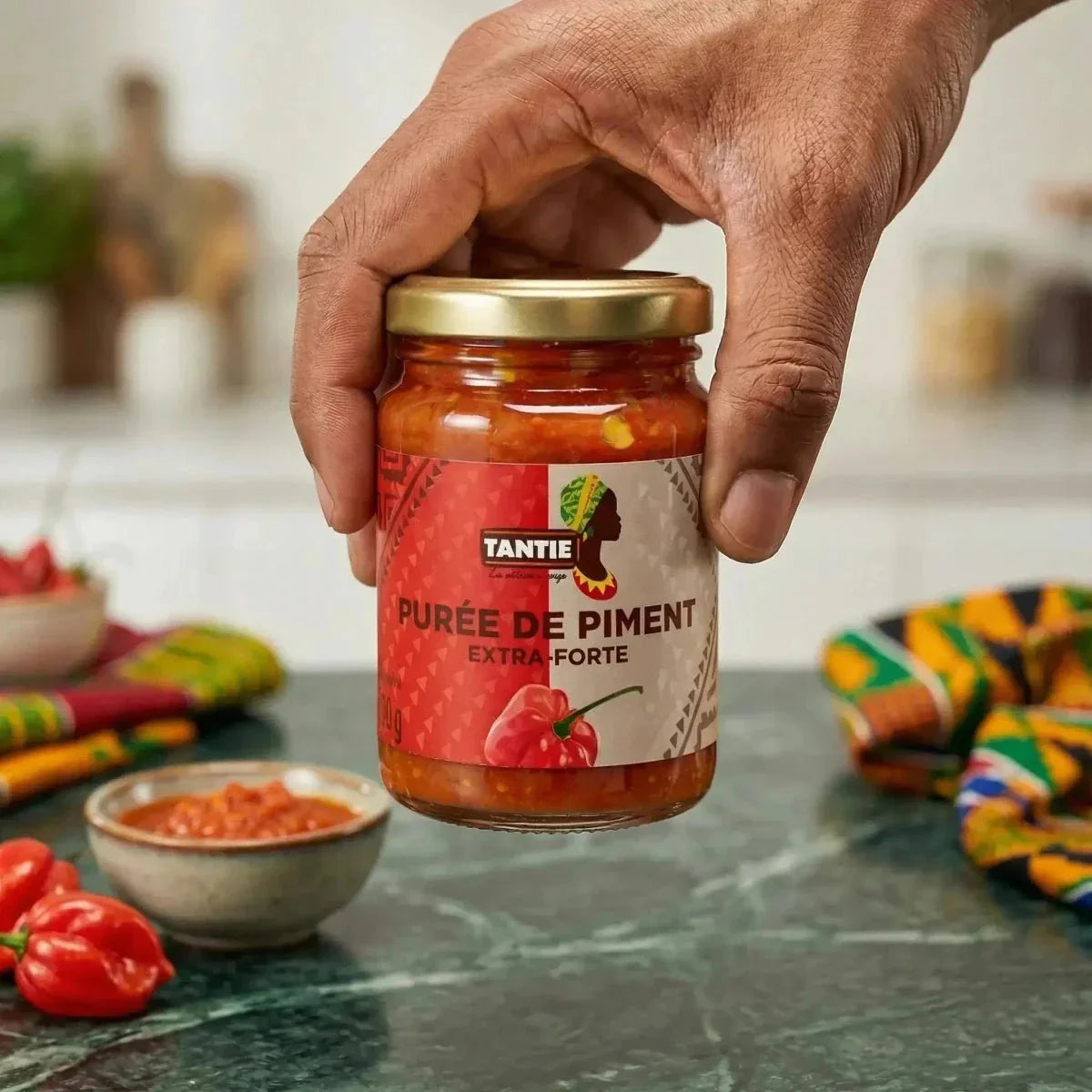 Purea di peperoncini extra piccante TANTIE 100g presentata a mano, con peperoncini e ciotola di purea come decorazione.