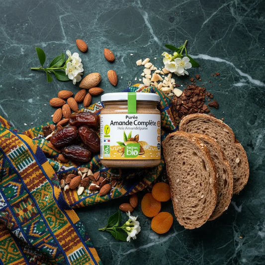 Purée d'amande complète RACINES BIO entourée d'ingrédients naturels comme dattes, amandes et pain complet, parfaite pour recettes sucrées bio.