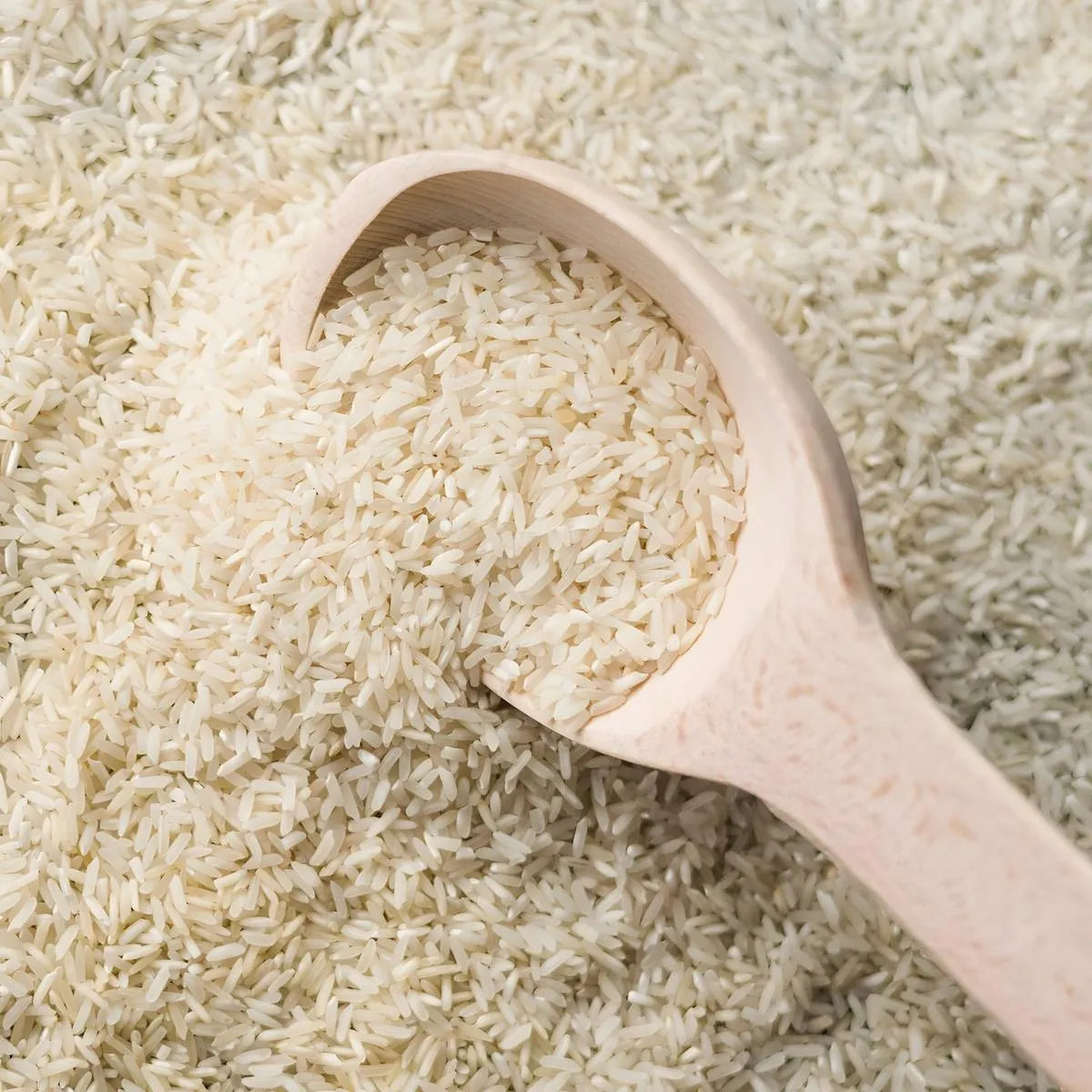 Gros plan sur grains de Riz Basmati TILDA dans une cuillère en bois, texture fine et allongée parfaite pour plats raffinés.