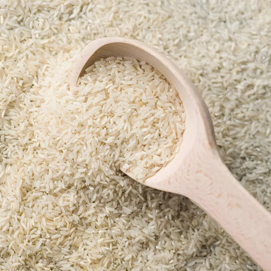 Gros plan sur grains de Riz Basmati TILDA dans une cuillère en bois, texture fine et allongée, parfait pour cuisine savoureuse.