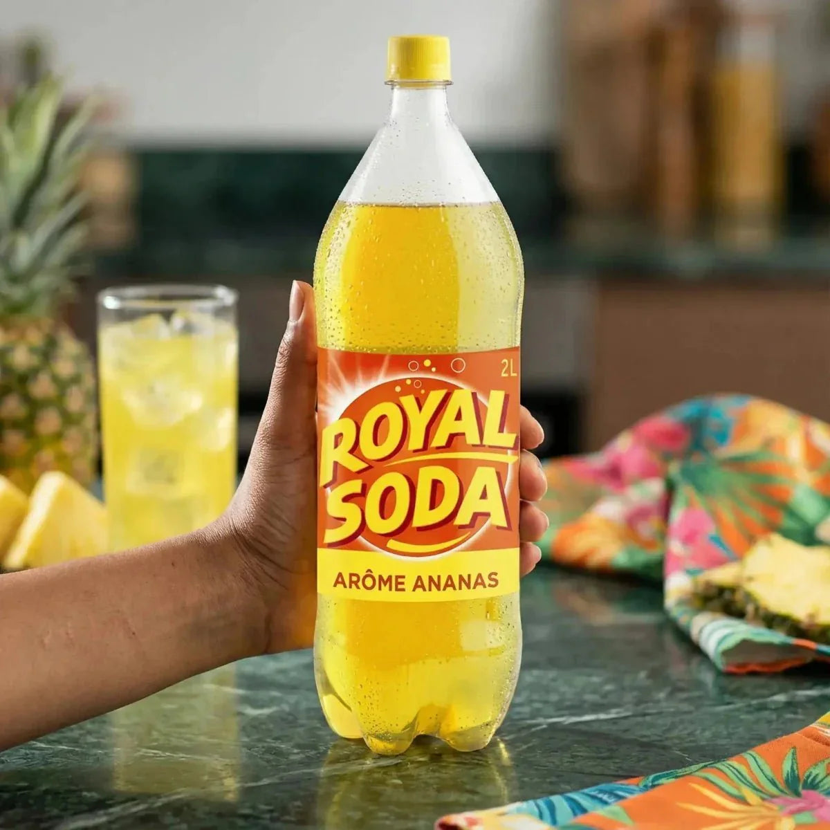 ROYAL SODA, refresco sabor piña en botella de 2L, sostenida a mano, con un vaso lleno.