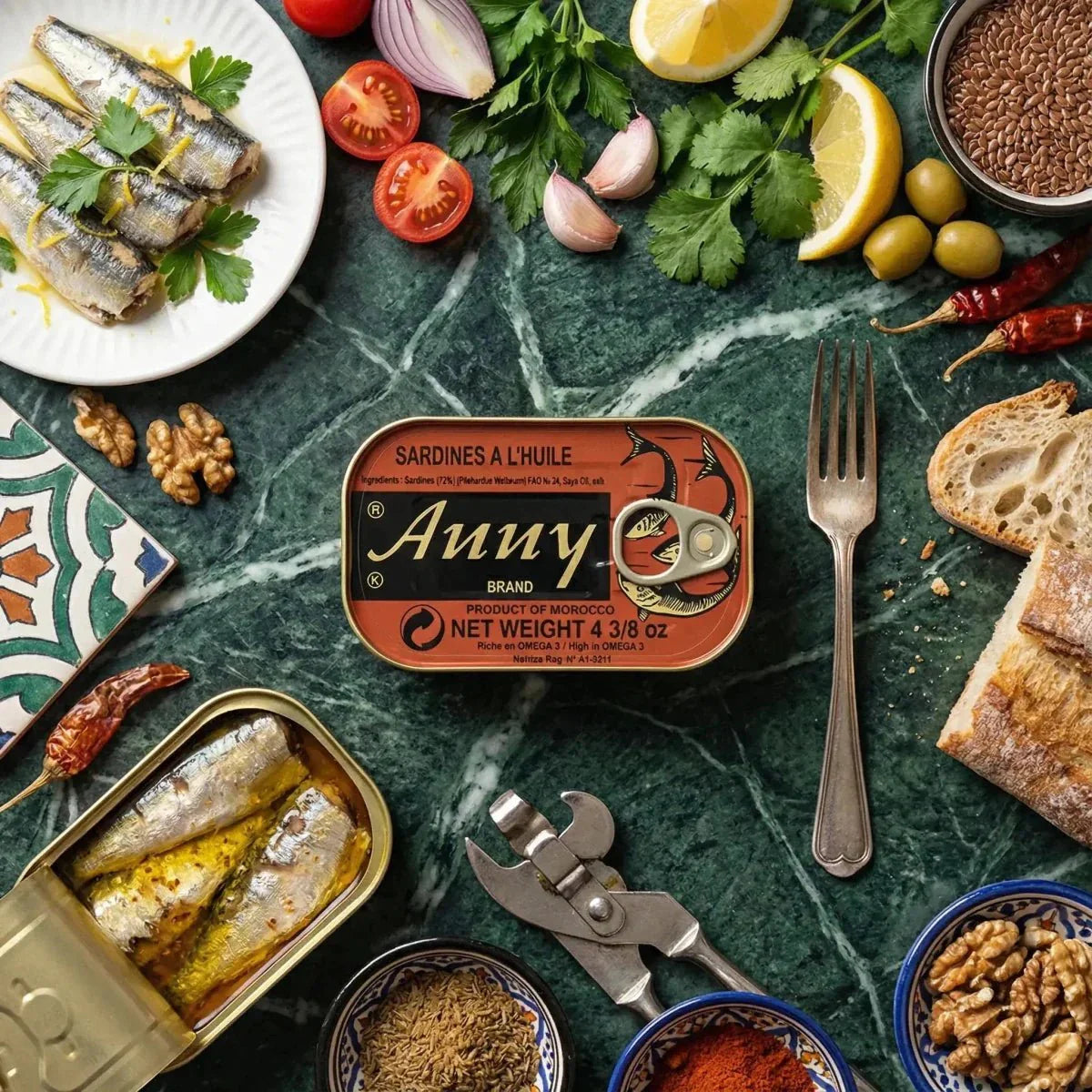 ANNY sardines in oil on a marble table with bread, vegetables, spices, and kitchen accessories.