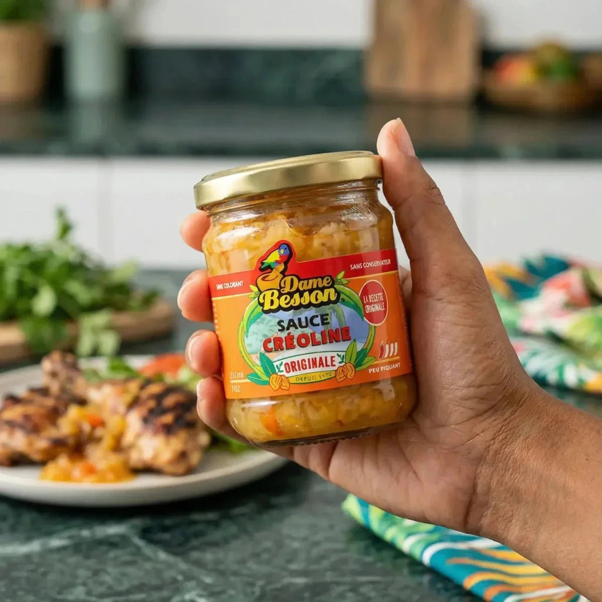 Creole sauce by Dame Besson, in a golden glass jar, held in hand.