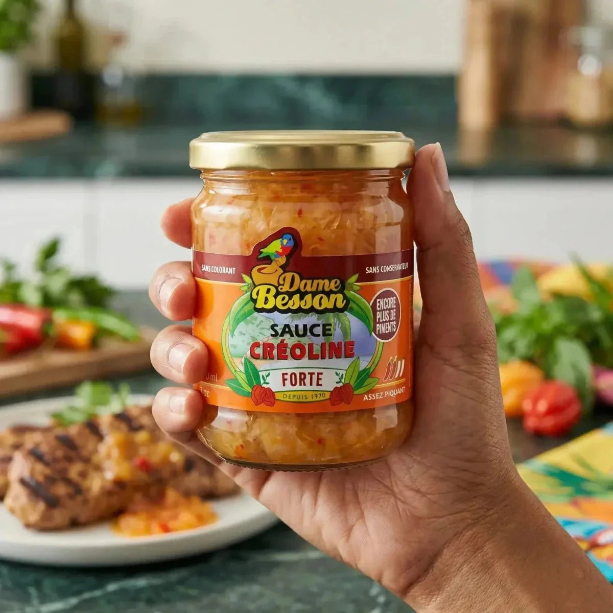 Sauce créoline forte par Dame Besson, en bocal de verre, avec des légumes en arrière-plan.
