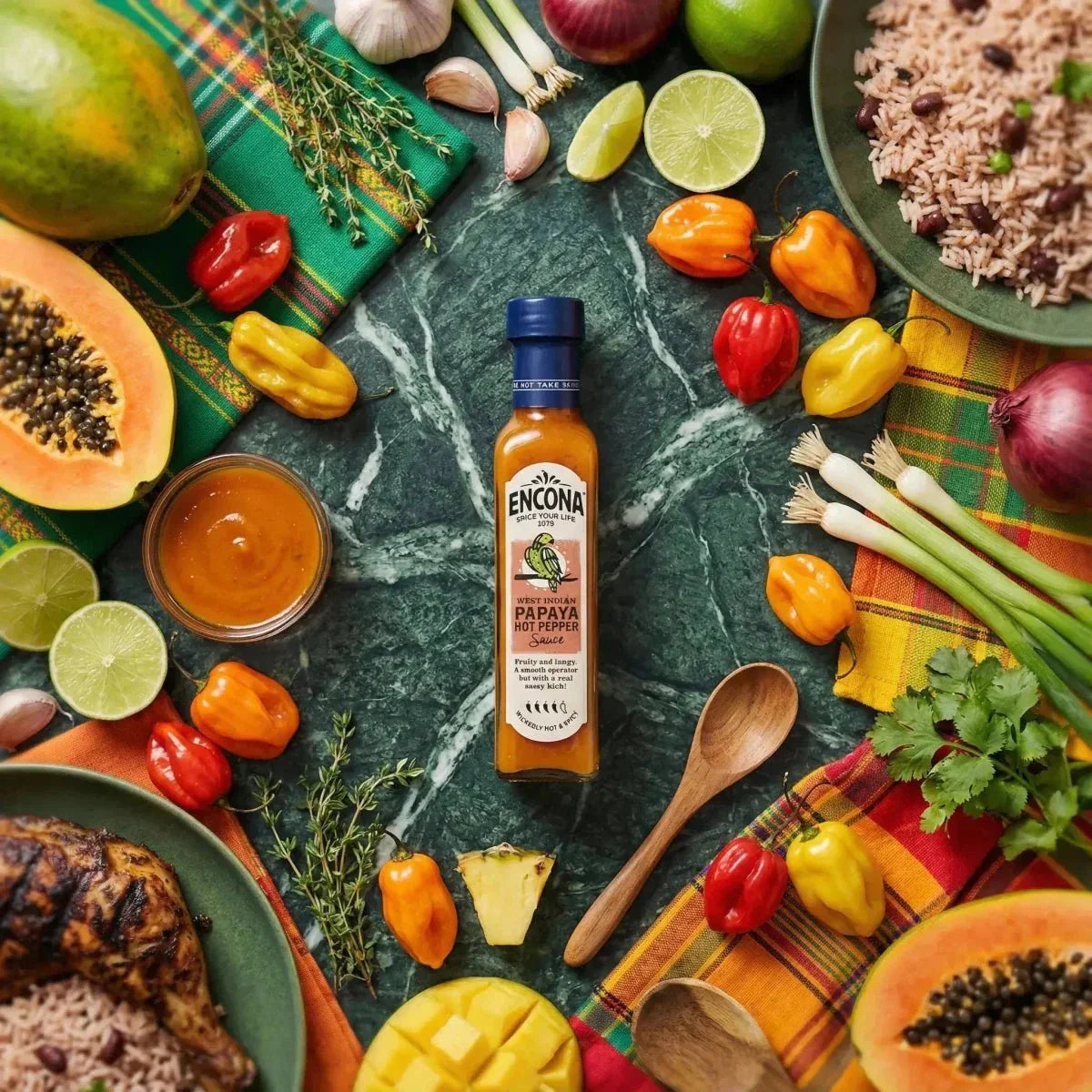 Sauce piquante à la papaye des Antilles par Encona, parmi des fruits frais et des épices colorées.
