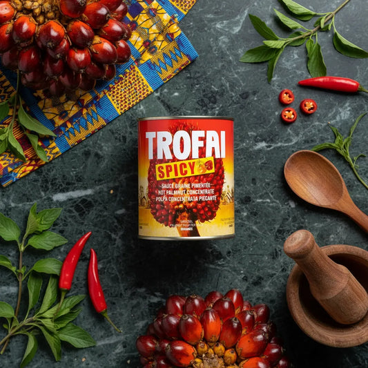 Boîte de Sauce Graine de Palme Spicy TROFAI posée sur table avec piments rouges, feuilles fraîches et régimes de palme, ambiance culinaire africaine.