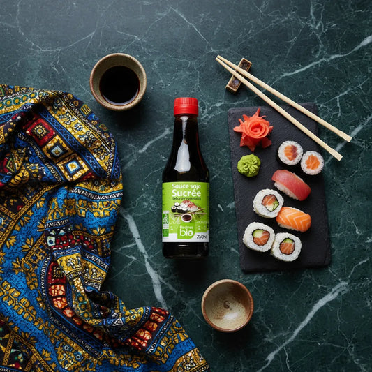 Sauce soja sucrée RACINES BIO posée à côté de sushis sur table en marbre, idéale pour accompagner plats asiatiques avec une touche sucrée bio.