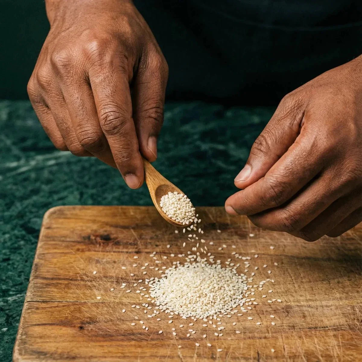 Sésame blanc SAMIA. Mains saupoudrant les graines d'une cuillère en bois sur une planche à découper.