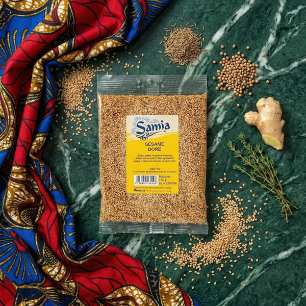 Tüte mit goldenem Sesam SAMIA auf grün marmoriertem Hintergrund, umgeben von Gewürzen, Ingwer und Thymian.