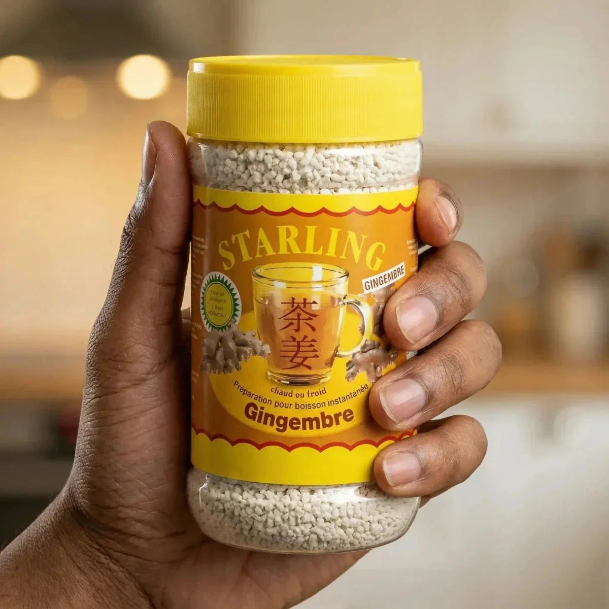 Sterling gemberthee in de hand gehouden. Gele pot, gemberdetails. Keuken op de achtergrond.