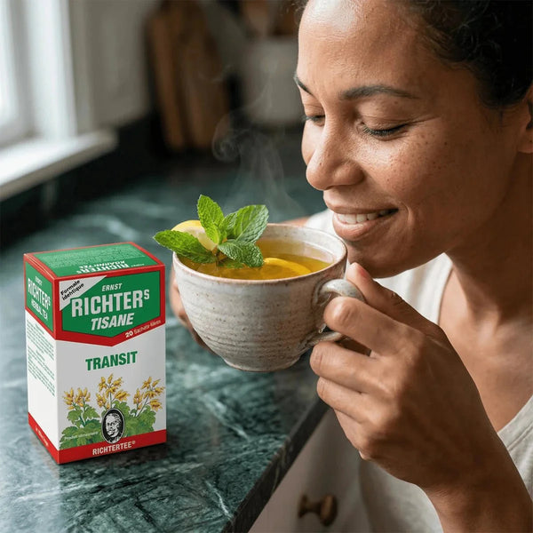 Tisane Transit Richter : femme appréciant une tasse de thé fumant, boîte de tisane à côté.