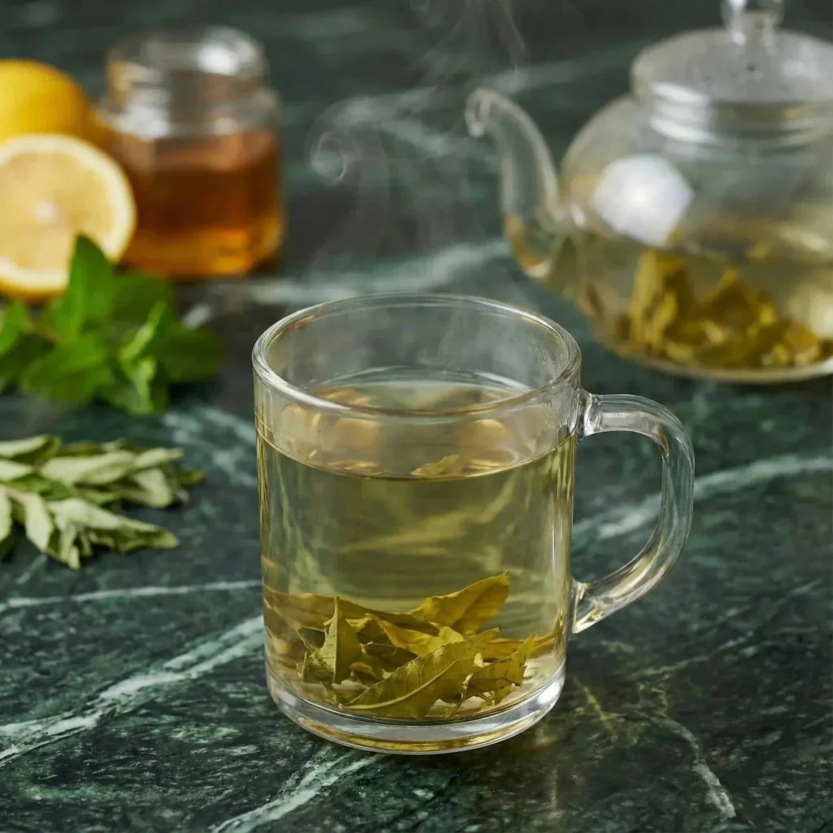 Verveine SAMIA: dampende kruidenthee in een kopje, citroenverbena bladeren, theepot, citroen en pot honing.