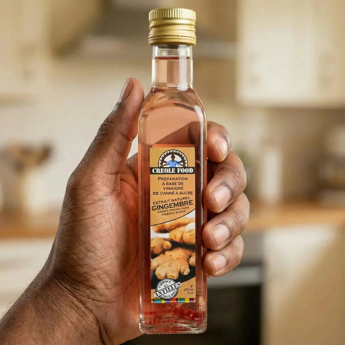 Vinaigre de canne au gingembre de CREOLE FOOD, en bouteille de verre, tenu dans une main.