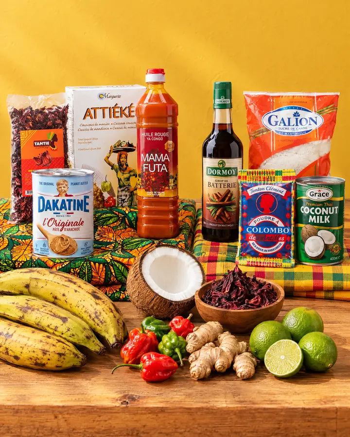 Étal du marché NKOSI : l’Afrique sur un wax (bissap TANTIE, attiéké, Dakatine, huile de palme Mama Futa), les Antilles sur un madras (sirop de batterie Dormoy, sucre Le Galion, colombo, lait de coco), avec plantains, piments, gingembre et citrons verts